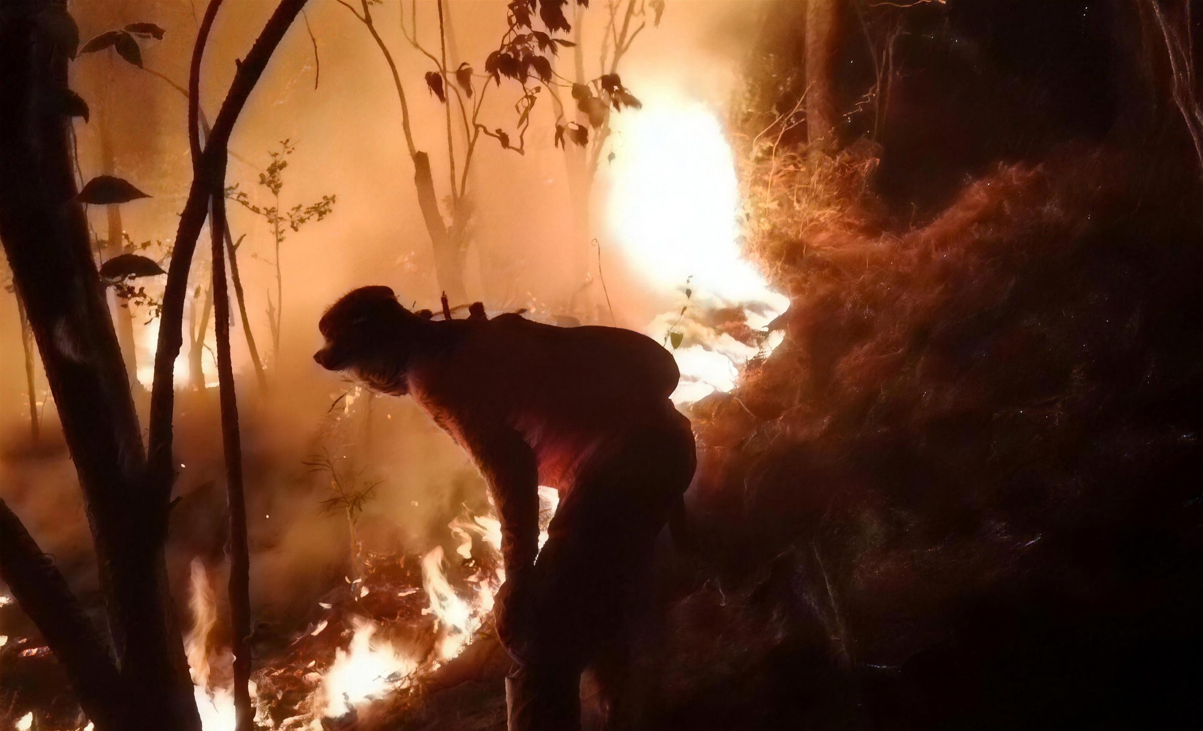 A firefighter bent over flames on a dark forest slope
